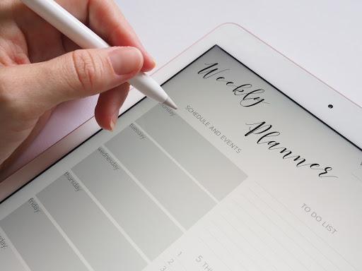 writing in a weekly planner on a tablet